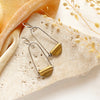 The pinned brass earrings styled on a rock with orange velvet and dried grass