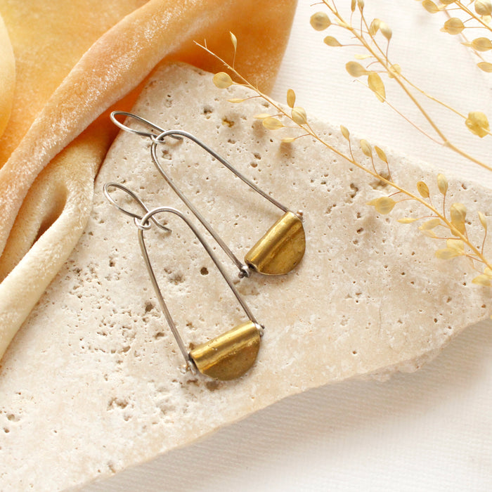 The pinned brass earrings styled on a rock with orange velvet and dried grass