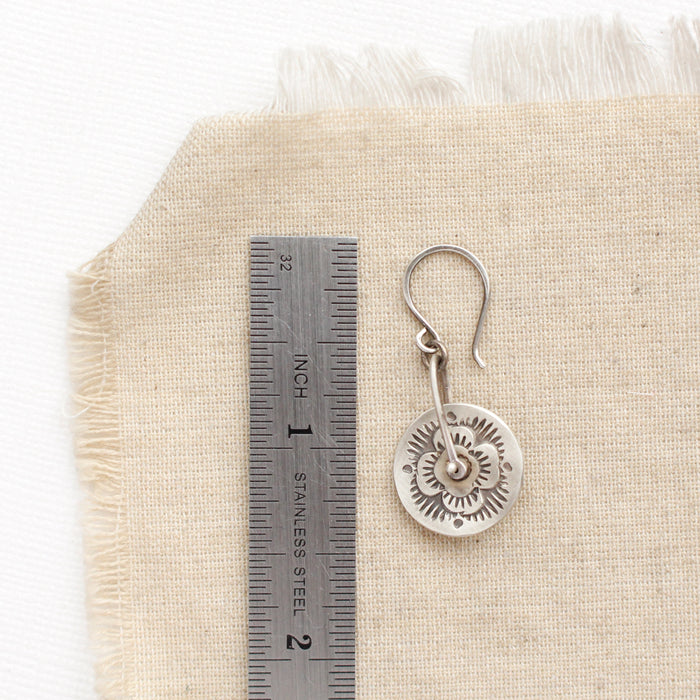 A pinned columbine disc earring next to a ruler for size reference