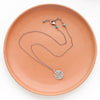 The pinned columbine disc necklace styled on an orange plate to show the adjustable lobster clasp closure