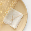 The pinned gold herkimer diamond necklace styled on a tan plate with linen and dried grass