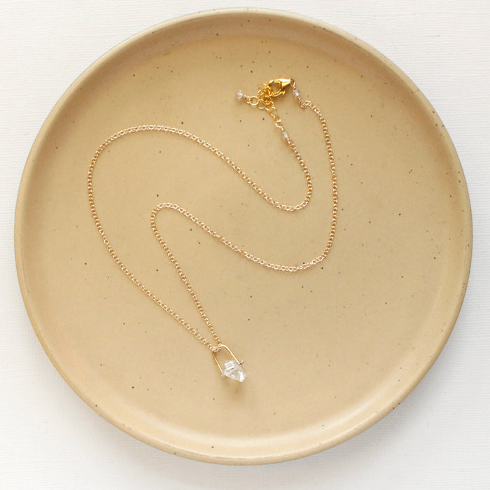 The pinned gold herkimer diamond necklace styled on a tan plate to show the adjustable lobster clasp closure