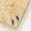 The lapis spear earrings styled on a tan rock with linen and dried grass
