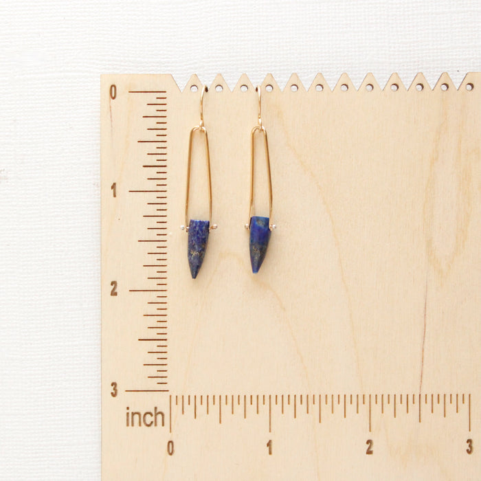 The lapis spear earrings on a wooden ruler to show size reference