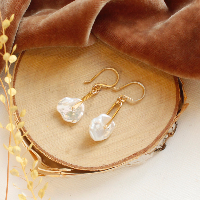 The pinned organic pearl earrings styled on wood with orange velvet and dried grass