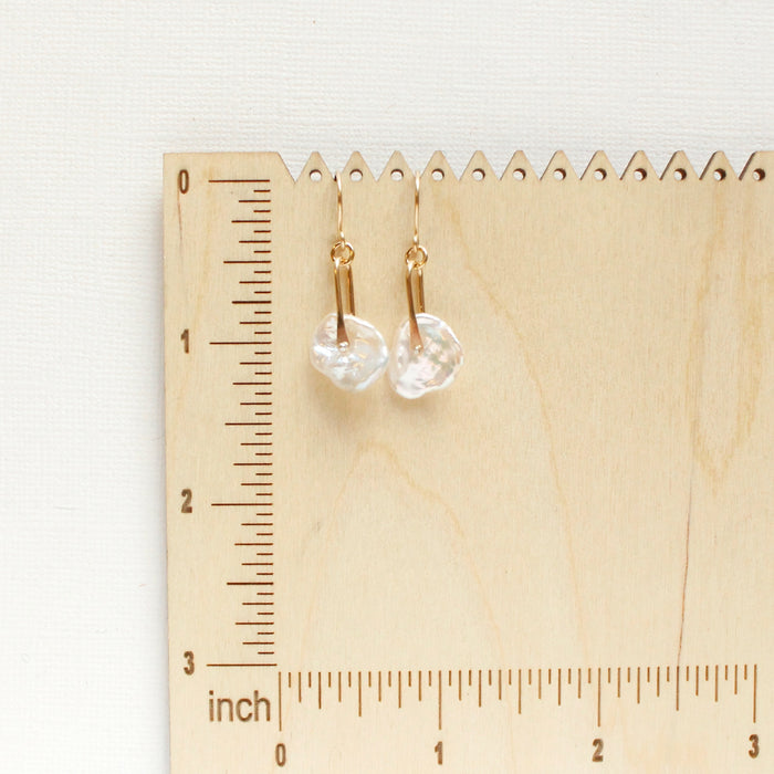 The pinned organic pearl earrings on a wooden ruler for size reference