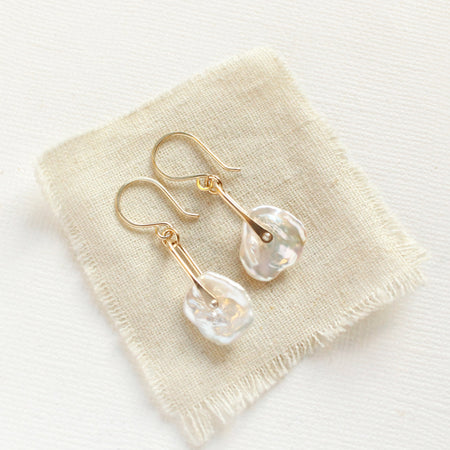 The pinned organic pearl earrings styled on tan linen