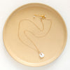 The pinned organic pearl necklace styled on a tan plate to show the adjustable lobster clasp closure