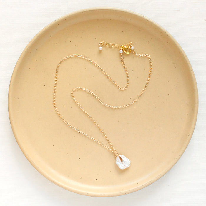 The pinned organic pearl necklace styled on a tan plate to show the adjustable lobster clasp closure