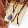 The pinned sodalite adjustable leather necklace styled on a tan rock with orange velvet