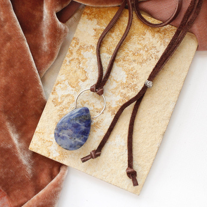 The pinned sodalite adjustable leather necklace styled on a tan rock with orange velvet