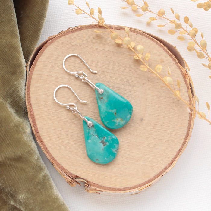 The pinned turquoise earrings styled on wood with green velvet and dried grass