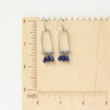 The pinned vinca arch earrings on a wooden ruler for size reference