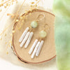 The prehnite and pearl chandelier earrings styled on wood with linen and dried grass