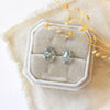 The prong set aquamarine post earrings styled on a velvet box with tan linen and dried grass