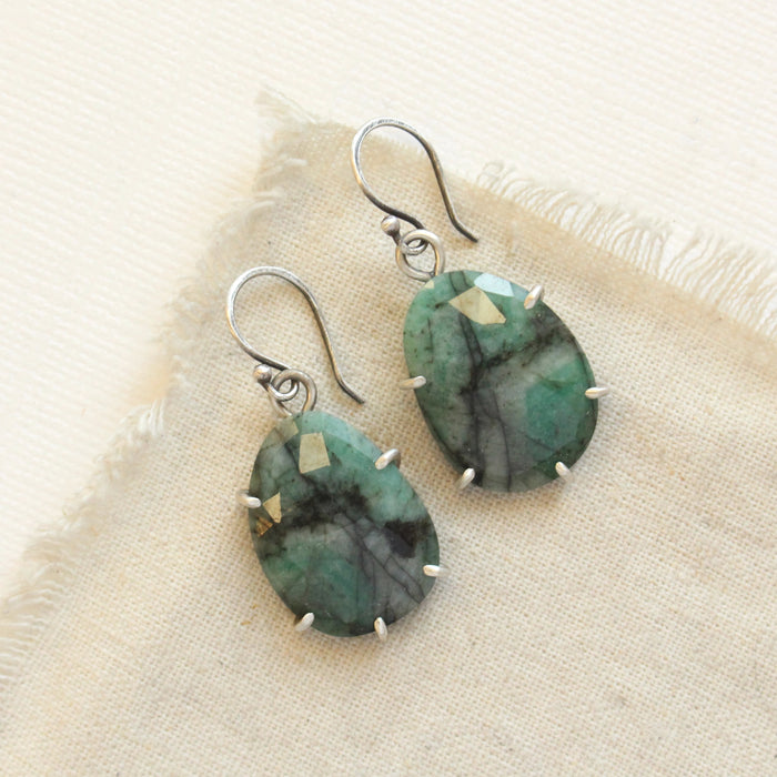 The prong set emerald earrings styled on tan linen