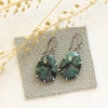 The prong set emerald earrings styled on gray leather with dried grass