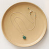 The prong set emerald necklace styled on a tan plate to show the adjustable lobster clasp closure
