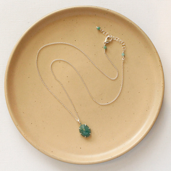 The prong set emerald necklace styled on a tan plate to show the adjustable lobster clasp closure