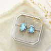 The lavender turquoise post earrings styled on tan linen with dried grass