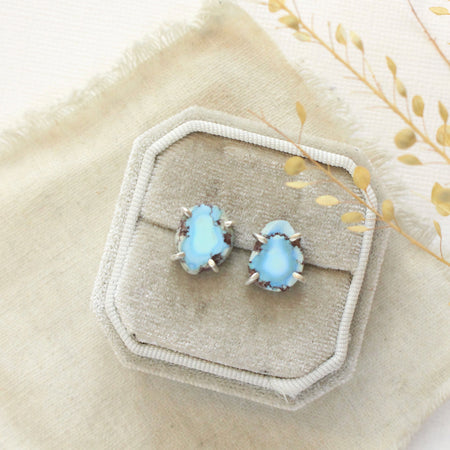 The lavender turquoise post earrings styled on tan linen with dried grass
