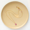 The prong set ruby necklace styled on a plate to show the adjustable lobster clasp closure