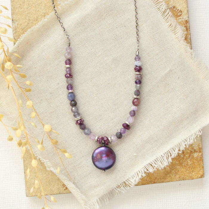 The purple rain necklace styled on a tan rock with linen and dried grass