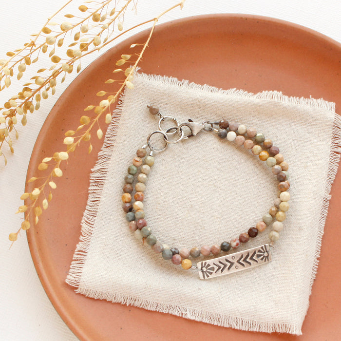 The rainbow agate sun bar double strand bracelet styled on an orange plate with linen and dried grass