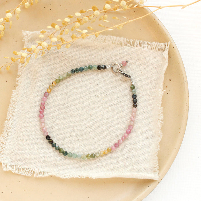 The rainbow tourmaline bracelet styled on a tan plate with linen and dried grass
