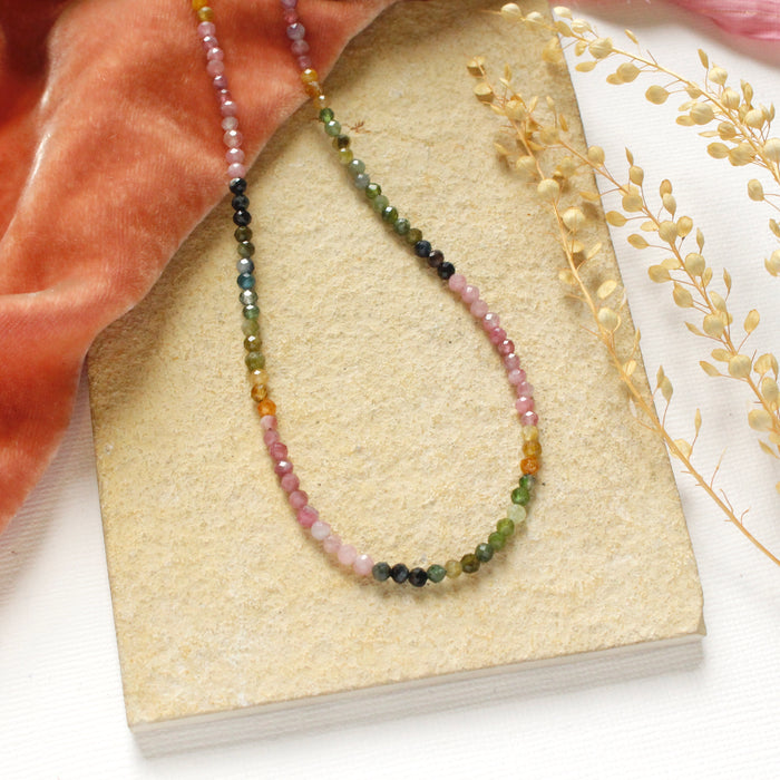 The rainbow tourmaline necklace styled on a tan rock with orange velvet and dried grass