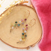 The rainbow vine earrings styled on wood with pink velvet and dried grass