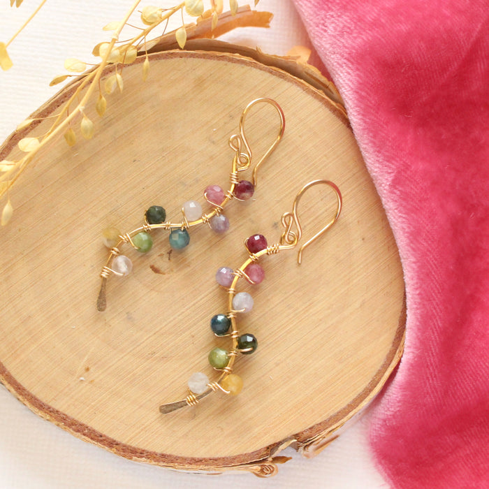 The rainbow vine earrings styled on wood with pink velvet and dried grass