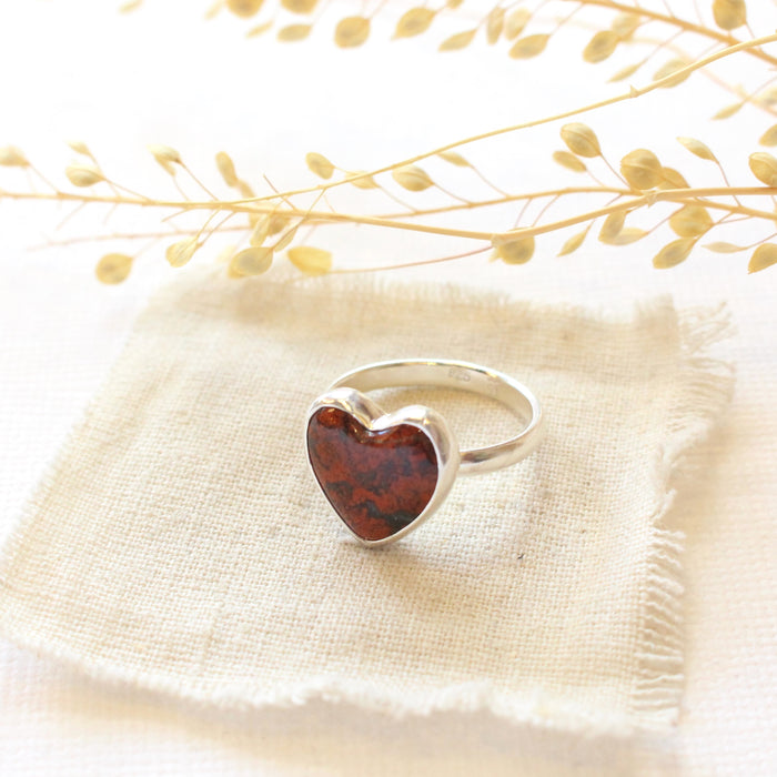 The red jasper heart ring styled on tan linen with dried grass