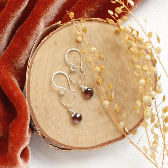 The rhodolite garnet silver hoop earrings styled on wood with orange velvet and dried grass