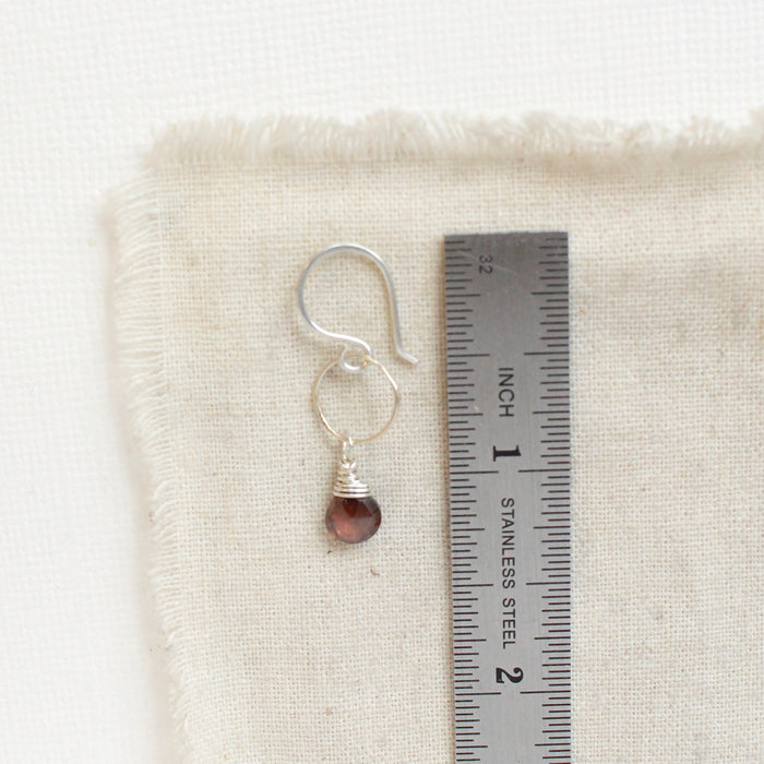 A rhodolite garnet silver hoop earring next to a ruler for size reference