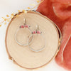 The rhodonite halo hoop earrings styled on wood with coral velvet and dried grass