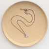 The rhodonite and sprout charm necklace styled on a tan plate to show the adjustable lobster clasp closure