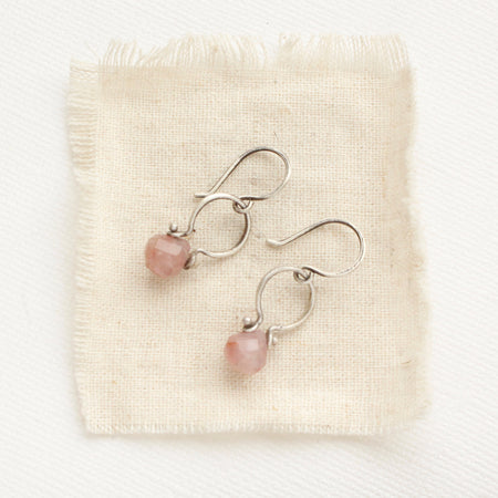 The madagascar rose quartz la cloche earrings styled on tan linen