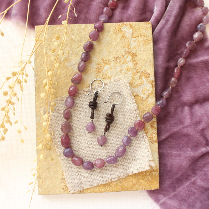 The ruby and leather earrings styled on on a tan rock with the matching necklace