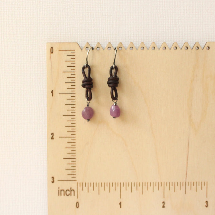 The ruby and leather earrings on a wooden ruler for size reference
