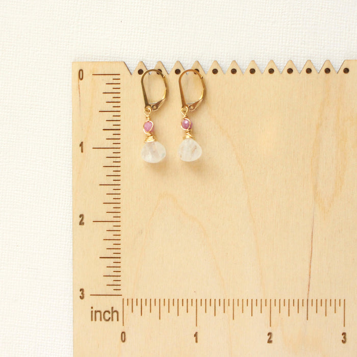 The ruby and moonstone drop earrings on a wooden ruler for size reference