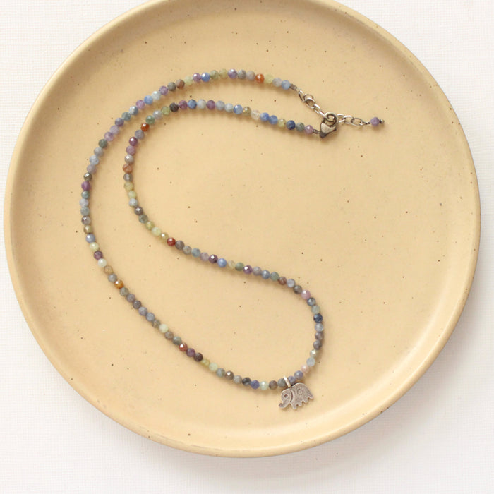 The sapphire and elephant necklace styled on a tan plate to show the adjustable lobster clasp closure