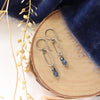 The sapphire hoop earrings styled on wood with blue velvet and dried grass