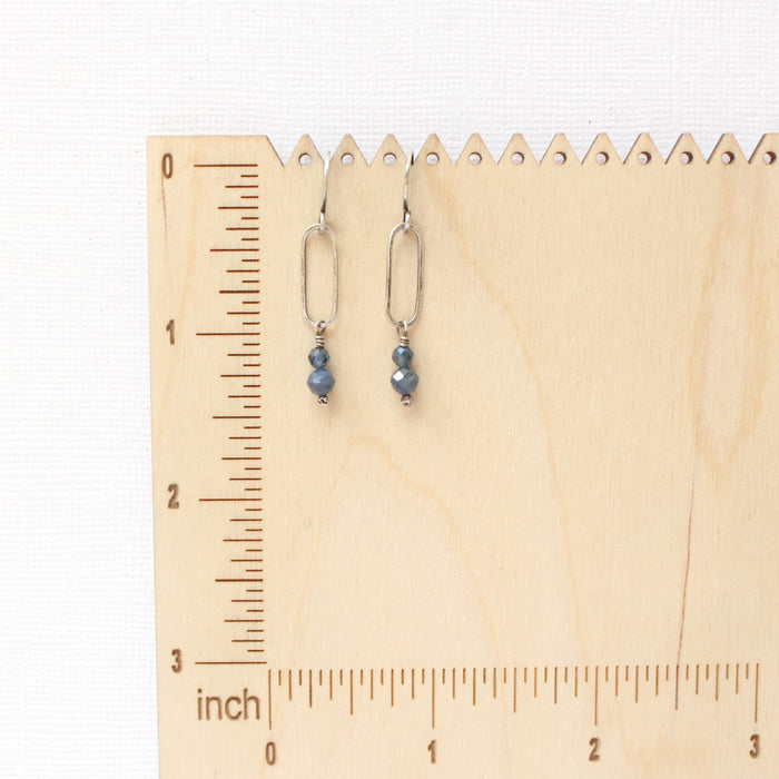 The sapphire hoop earrings on a wooden ruler for size reference