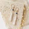 The sapphire and pearl earrings styled on a tan rock with linen and dried grass
