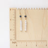 The sapphire and pearl earrings on a wooden ruler for size reference