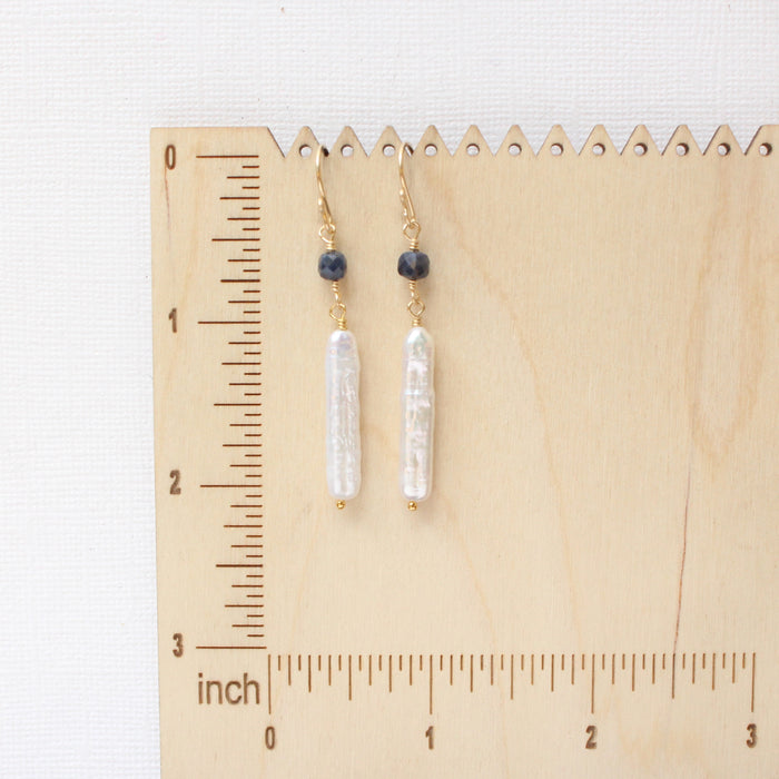 The sapphire and pearl earrings on a wooden ruler for size reference