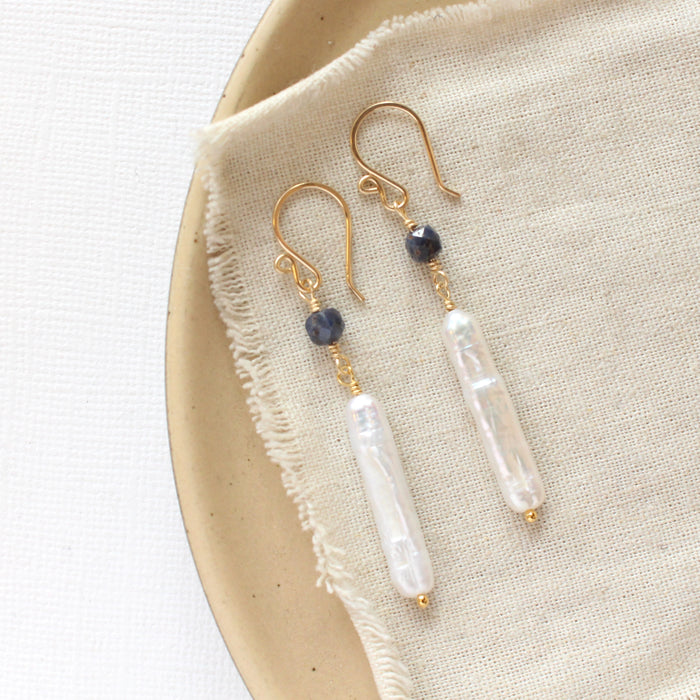 The sapphire and pearl earrings styled on a tan plate with linen