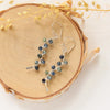 The sapphire wrapped silver vine earrings styled on wood with dried grass