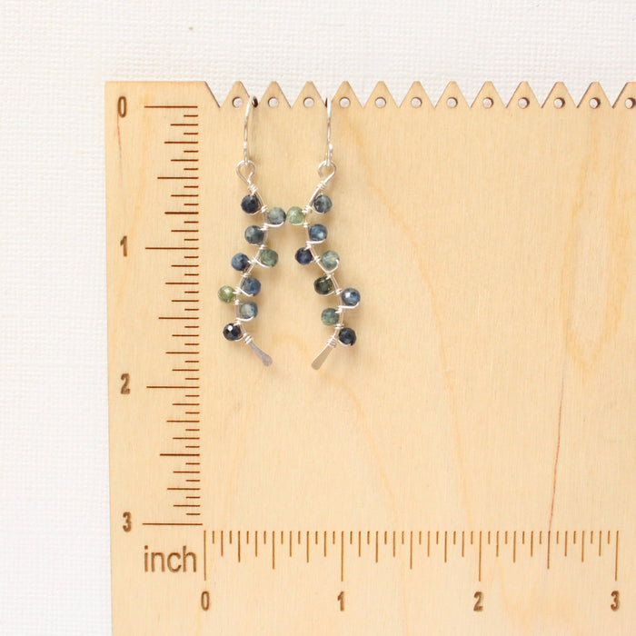 The sapphire wrapped silver vine earrings on a wooden ruler for size reference